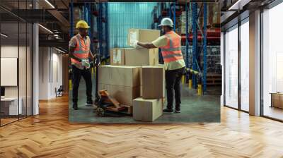 Two African American warehouse workers working together in warehouse moves cardboard boxes using manual pallet Truck. Wall mural