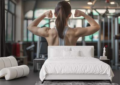  a young woman flexing her arms and back muscles, standing in a gym interior. Wall mural