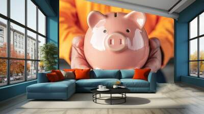 A person holding a pink piggy bank, symbolizing saving and financial planning in a vibrant orange shirt. Wall mural