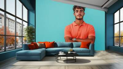 Full body shot of a young attractive Brazilian man dressed in a classic polo shirt and casual shorts standing with a curious contemplative expression against a plain sky blue studio background Wall mural