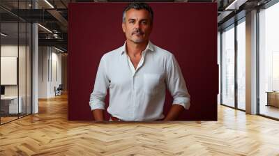 Portrait of a Determined Middle aged Brazilian Man Dressed in a Crisp Button down Shirt and Chinos Posing Confidently against a Burgundy Studio Backdrop with Dramatic Lighting Wall mural