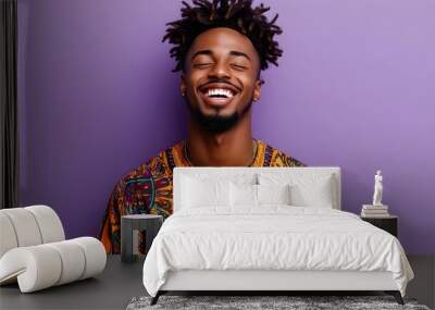 Portrait of a happy and joyful young African American man wearing a vibrant patterned dashiki ethnic clothing against a plain lavender studio background with ample copy space above Wall mural