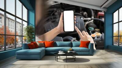 Close-up of woman's hands holding smartphone with empty space on screen for your text, background of car engine. Wall mural