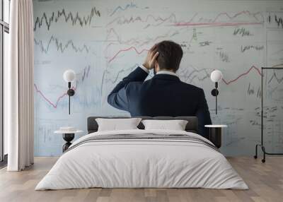 A businessman analyzing complex data charts on a wall, depicting financial trends and market analysis in an office setting. Wall mural