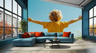 A carefree child enjoying nature, arms outstretched, embracing freedom under a clear blue sky. Wall mural