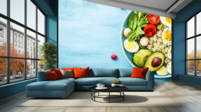 Fresh salad bowl with avocado, eggs, tomatoes, and greens on a light blue table. Wall mural