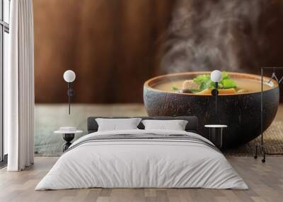 Steaming bowl of soup with fresh herbs on wooden table. Wall mural