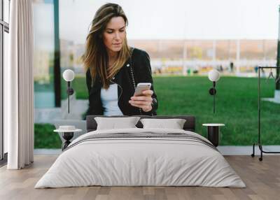 Successful business woman reading email on a mobile phone while sitting with a portable computer on her knees. Student girl using smartphone and a laptop connected to wifi to participate in webinar Wall mural