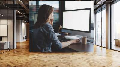 view from back to female student is talking on smartphone sitting at desk in front of monitor with blank space for design. Mockup screen with copy space. woman makes a business call Wall mural