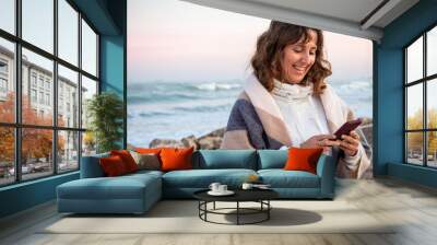 Happy baby  boomer woman with a blanket on the beach looking at her mobile phone Wall mural