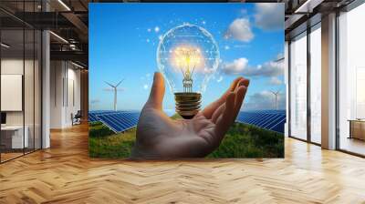 Hand holding a light bulb in a landscape with windmills and solar panels. Clean energy concept, renewable energy and ecology. Sustainable development through alternative energies. Wall mural