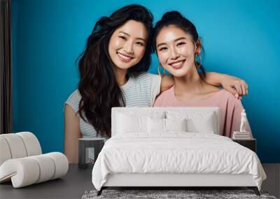 Two Asian girls smiling and hugging on blue background. Best friends or female partner, free and inclusive friendship and love. Wall mural