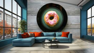 Pink glazed donut with sprinkles on a black and green plate,, on a wood table. Wall mural