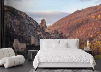 The ruins of the Lednica castle standing on a limestone rock. In the background there is an autumn forest and a sky with clouds. Wall mural