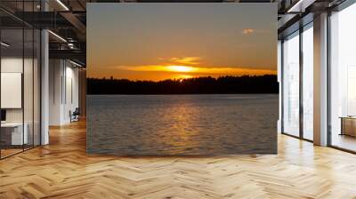 Beautiful sunset moment at the lake. Sun glowing on the water surface and behind the forest. Wall mural