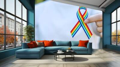 hand showing LGBTQ Rainbow ribbon against sky background in the morning. Support Lesbian, Gay, Bisexual, Transgender, Queer community and Rights concept Wall mural