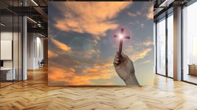 Silhouette hand holding wood cross against sunrise background, open palm up worship, pray for blessings from God. Christian Religion, Crucifix and Faith concept Wall mural