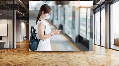 young Asian girl wearing Surgical face mask protect coronavirus inflection, Happy tourist woman using smartphone during walking in subway station. new normal and life after covid-19 pandemic Wall mural