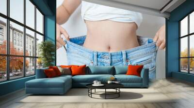 young slim female wearing big or oversize jeans, woman show healthy shape after weight loss. dieting, exercise, body fit and liposuction surgery concept Wall mural