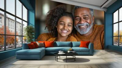 A father with graying hair enjoys a joyful moment with his smiling daughter on a cozy couch in their living room in the afternoon light Wall mural