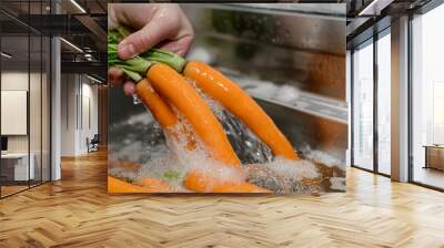 A hand washes carrots under running water in a kitchen sink. Wall mural