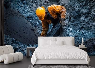 A miner in an orange shirt and helmet extracts coal from a dark, rocky pit during the early morning hours Wall mural