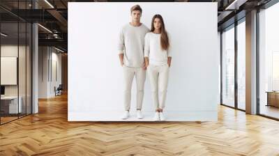 a young couple poses on a white background, wearing white casual clothes, models posing. Wall mural