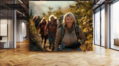 Woman with a prosthetic leg joyfully hiking along a scenic mountain trail in the afternoon sun with fellow adventurers nearby Wall mural