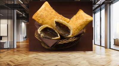 Tradional Brazilian fried pastry called pastel stuffed with chocolate Brazilian dessert brigadeiro with one open in a basket in wood background Wall mural