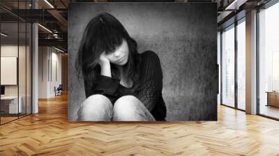 Black and white photo of a sad anonymous young woman who is thoughtful about troubles in front of a gray wall Wall mural