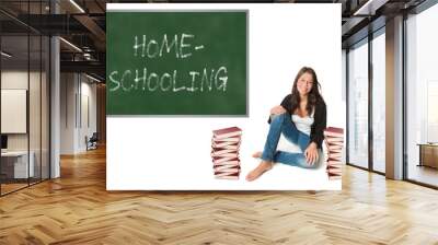 Happy schoolgirl between two huge piles of books in front of a chalkboard, homeschooling is written on the board, isolated on white studio background Wall mural