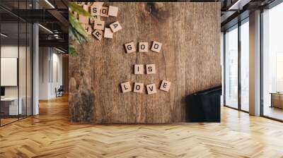 God is love spelled in block letters on a wooden table with a bible and a plant. Wall mural