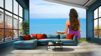 Beautiful fit young woman mediating by the ocean Wall mural