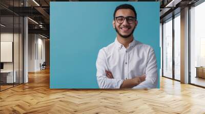 Smiling confident arab young man, male student, professional employee or programmer standing isolated on blue background. Happy handsome ethnic guy wearing shirt and glasses, Generative AI. Wall mural