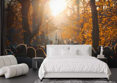 A solemn gathering of people at a funeral service in a cemetery during autumn, with sunlight filtering through trees. AI Wall mural