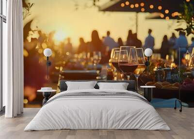 Close-up of a sunset dining setup outdoors, featuring glasses of wine and plates of gourmet food with people socializing in the background. Birthday, corporate party celebration. Wall mural