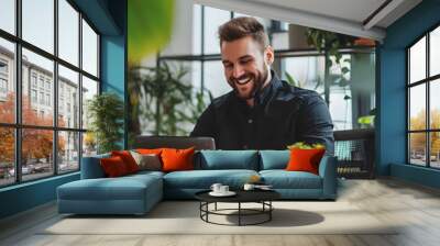 finance employee sitting at his desk in his office and looking at the phone in his hand, a smiling person Wall mural