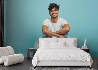 Full body young happy Indian man he wear white t-shirt casual clothes sit in bag chair hold hands crossed folded isolated on plain pastel light blue cyan background studio portrait. Lifestyle concept. Wall mural