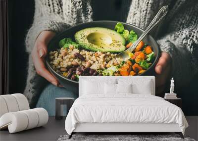 Healthy vegetarian dinner. Woman in jeans and warm sweater holding bowl with fresh salad, avocado, grains, beans, roasted vegetables, close-up. Superfood, clean eating, vegan, dieting food    Wall mural