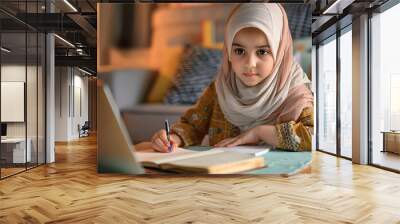 Little Muslim girl in hijab doing homework at home Wall mural