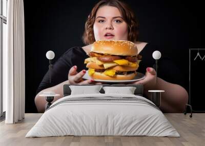 Plus size fat woman in black dress with hamburger on black background. Overweight. Overeating Concept. Obesity Concept with Copy Space. Wall mural