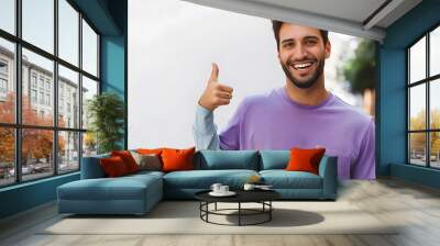 Outgoing, happy handsome hipster man pointing left, showing where get excellent tourist trip offer to have journey on holidays. Satisfied smiling man in purple t-shirt recommend promo Wall mural