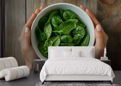 Overhead shot of white bowl with fresh organic spinach held by white female hands on wooden table Wall mural