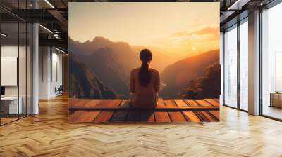 Picture from the back of a woman sitting on wooden porch extending into a high mountain cliff. The sun is setting on the mountain and there is a beautiful warm orange light. The traveling background. Wall mural