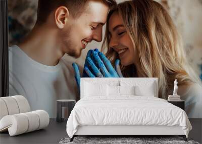 Smiling young pretty couple with fair hair stand closing eyes, nuzzling noses, showing hands covered with blue paint. Wall mural