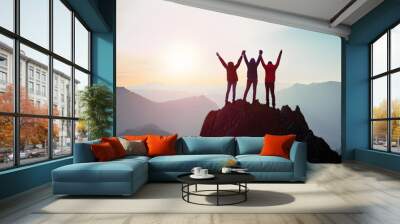 Together overcoming obstacles with three people holding hands up in the air on mountain top , celebrating success and achievements Wall mural