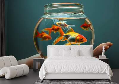 Woman's hand holds small aquarium fishbowl with goldfish on dark background. Wall mural