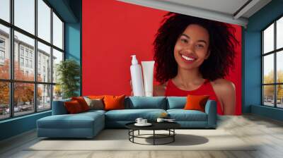 young black woman hold blank shampoo bottle and conditioner for hair on red background, smiling woman portrait, moisturizing spa body care bodycare concept Wall mural