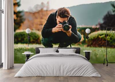 Young man crouching while using camera on lawn Wall mural