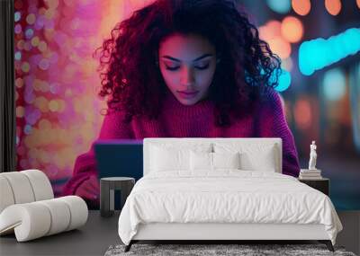 Young woman with curly hair using a laptop outdoors with colorful neon lights in the background Wall mural